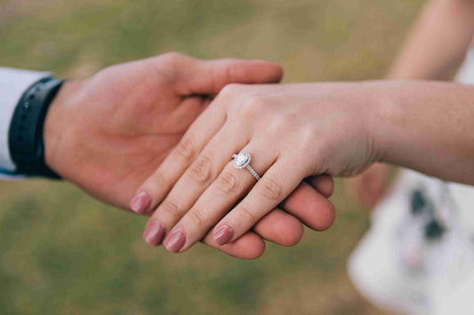 Close-up of a couple holding hands, showcasing an elegant diamond engagement ring on the woman's hand.